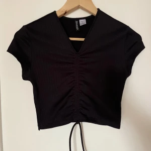Svart croppad topp från H&M  - Svart croppad topp från H&M med korta ärmar och v-ringning. Toppen har snörning framtill, säljer då den inte kommer till användning längre🤍