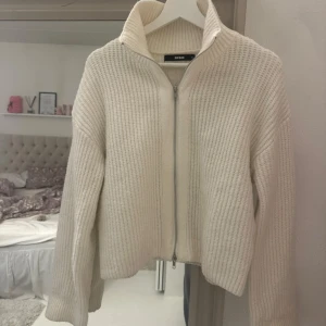 Vit stickad kofta från Bik Bok - Supermysig vit stickad kofta från Bik Bok med hög krage och dragkedja framtill. Den har en ribbad struktur och långa ärmar, perfekt för lager-på-lager under kyliga dagar. Enkel att matcha och ger en clean vibe till din outfit.