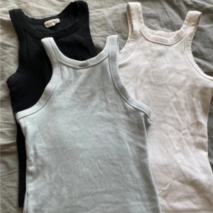 3-pack ribbade linnen - Tre ribbade linnetoppar i svart, vit och ljusblå. Alla är ärmlösa med klassisk rund halsringning och tight passform. Säljes som paket.