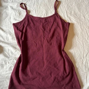 Vinröd linnetopp från Basic You - Enkel och snygg vinröd linnetopp från Basic You i ekologisk bomull. Modellen är ärmlös med smala axelband och har en rak, figurnära passform. Perfekt att matcha med jeans eller kjol för en chill look.