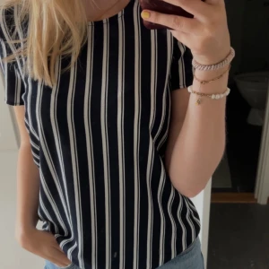 Randig topp från Vero Moda XS - Snygg svart och vit randig topp från Vero Moda i storlek XS. Modellen har korta ärmar, rund halsringning och en dragkedja bak. Materialet är strukturerat och känns lite tjockare, vilket ger en cool look. Perfekt till jeans eller kjol.