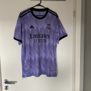 Real Madrid Kroos 8 Adidas tröja L - Säljer en officiell Real Madrid fotbollströja från Adidas i storlek L. Tröjan är ljuslila med svart tryck, har korta ärmar och ett grafiskt mönster. Kroos och nummer 8 på ryggen. Storleken är L så tröjan passar någon som är 175-180 cm lång. Den är helt oanvänd så den är i nyskick lappar sitter även kvar. Vid minsta fundering hör av dig.