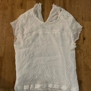 Vit blus med struktur från ONLY - Säljer en söt vit blus från ONLY i storlek 42. Blusen har korta ärmar med volangkant, diskret prickig struktur och v-ringning både fram och bak. Tunt, luftigt tyg som känns perfekt för varmare dagar. Supersnygg till jeans eller kjol!