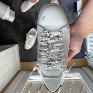 Vita sneakers från Oliver Cabell strl 40 - Snygga oanvända vita sneakers från Oliver Cabell (Sea Salt Ghost) i storlek 40. Ordinarie pris går på 250€ + frakt ca 30€ + tull 50€. Skorna har klassisk låg profil, rund tå och platt sula. Tillverkade i skinn med svarta detaljer på hälen och perforeringar på sidan. Tjocka vita snören med logga ger en clean och modern vibe. 