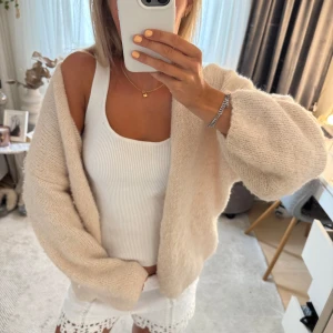 Beige stickad kofta med knapp - Mysig beige stickad kofta med en knapp framtill som jag sytt på själv. Koftan har en loose passform och ballongärmar som ger en chill vibe. Perfekt att slänga över ett linne eller t-shirt. Enkel och stilren design utan mönster.