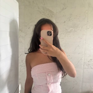 Ljusrosa bandeau tubtopp med knappar - Supersöt ljusrosa bandeau tubtopp med struktur och dekorativa pärlknappar framtill. Toppen är ärmlös och har en croppad passform som ger en trendig vibe. Perfekt för varma dagar och snygg att styla med jeans eller kjol. Aldrig använt