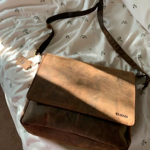 Brun axelväska i skinn från LEABAGS - Snygg brun axelväska från LEABAGS i äkta skinn med justerbar rem. Väskan har ett stort huvudfack, flera innerfickor och dragkedja baktill. Perfekt för laptop, böcker eller vardagsprylar. Stilren vintage-look och praktisk design. Priset kan diskuteras. 