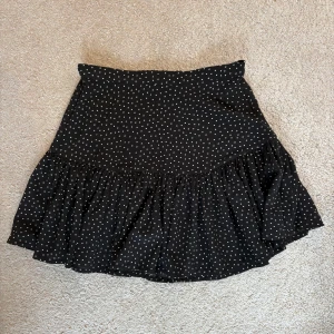 Svart prickig volangkjol Gina Tricot XS - Supersöt svart kortkjol från Gina Tricot med vita prickar och volangkant. 