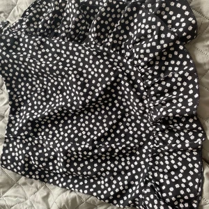 Svart blommig kjol med volang från SHEIN - Supersöt svart kortkjol från SHEIN med vita små blommor över hela tyget. Kjolen har volangkant nertill och en knyt-detalj i midjan. Perfekt för dig som gillar en feminin och trendig look. Materialet känns lätt och flowy.