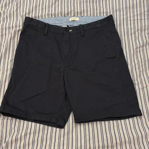 Svarta shorts från Gant - Klassiska mörkblå shorts från Gant med normal passform. De har fickor på sidorna, bälteshällor och knäppning fram. Materialet känns som bomull och de är perfekta för sommaren. Snygg och stilren look som funkar till det mesta.
