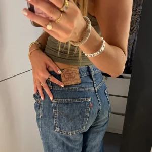 Levi's 501 blå jeans straight fit - Klassiska blå Levi's 501 jeans med rak passform och låg midja. Jeansen har fem fickor, knappgylf och den ikoniska läderpatchen bak. Perfekta för en avslappnad och tidlös look. Jag är 173. Byxorna är i superbraskick, bortsett från lappen som tyvärr sitter löst