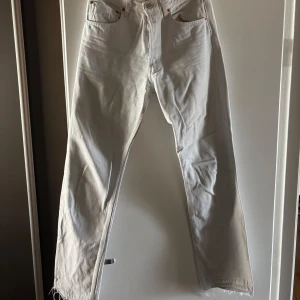 Vita Levi's 501 jeans med rå kant - Säljer ett par vita Levi's 501 jeans med klassisk rak passform och knäppning fram. Jeansen har råa, fransiga benslut för en cool och avslappnad vibe. Tillverkade i kraftig bomullsdenim och har fem fickor samt Levi's ikoniska patch bak.