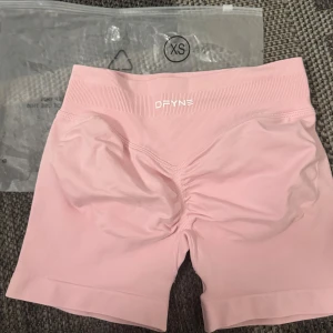 Rosa seamless shorts från DFYNE  - Säljer ett par ljusrosa seamless shorts från DFYNE i storlek XS. De har hög midja, ribbad linning och scrunch-detalj bak för extra form. Perfekta för träning eller chill dagar. Mjukt och stretchigt material som sitter skönt på kroppen.