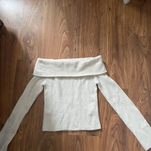 Offshoulder ribbad tröja från H&M - Superfin ljusvit ribbad stickad tröja från H&M med offshoulder-modell och långa ärmar. Tröjan har en bred krage som vilar snyggt över axlarna och ger en trendig look. Perfekt att styla med jeans eller kjol för en chill vibe.