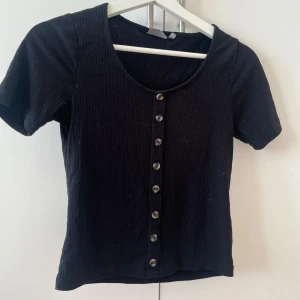 Svart ribbad topp med knappar - En svart ribbad topp med korta ärmar och snygga knappar längs hela framsidan. 