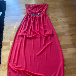 Röd axelbandslös långklänning Zara - Snygg röd axelbandslös långklänning från Zara Trafaluc med glittrig detalj i midjan. Klänningen har ett flowy fall och är perfekt för dig som vill sticka ut. Materialet känns lätt och svalt, och den glittriga dekoren ger extra wow-känsla.