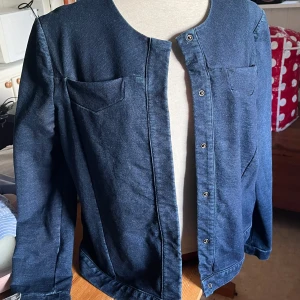 Mörkblå jeansjacka från COS - Snygg mörkblå jeansjacka från COS med minimalistisk design. Jackan har rundad halsringning, tryckknappar framtill och två bröstfickor. Nypris 1500kr.