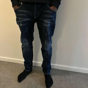Mörkblå jeans från Dsquared2 - Säljer ett par mörkblå jeans från Dsquared2 med snygga slitningar och tvättade detaljer. Jeansen har klassisk femficksdesign, raka ben och en relaxed fit. Perfekta för dig som gillar streetwear och vill sticka ut lite extra.