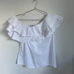 Topp - Topp med ena sidan som är off shoulder. Volanger på toppen. Passform: vid, A linje formad. Skick: som ny