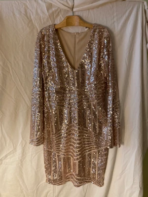 Festklänning i guld - Chic, knälång festklänning av märket DM Retro. Delvis transparent, delvis paljetter i guld. Fint v-ringat dekolletage. Blixtlås bak. Strl Large. Aldrig använd. Kostade 1375 kr