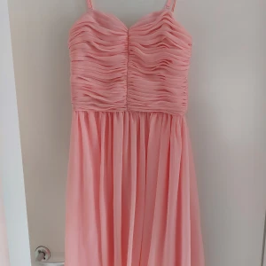 Klänning - Fin festlig apricos/laxrosa klänning. Överdelen är som ett korsettliv så man kan ha den utan något under. Axelbanden är avtagbar den är nedanför knän i längd. Fint skick från rök och djurfritt hem.