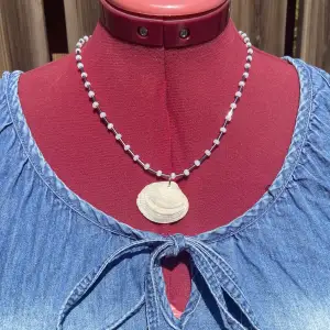 Fint somrigt hemmagjort halsband gjort med smyckeswire, glaspärlor och en snäcka! Mäter cirka 49-50 cm. OBS! Mät att halsbandet passar innan köp 