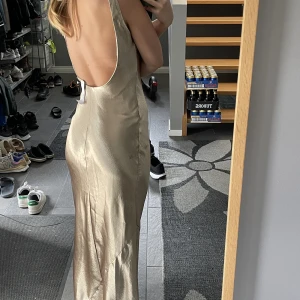 Maxiklänning i satin med djup ringning baktill - Helt ny klänning, aldrig använd. Champagnefärgad maxiklänning med så fin öppen rygg. 