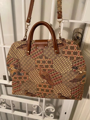 Retroväska gobeläng i suveränt skick – Ideal (Made in Sweden) - Svenskproducerad vintageväska från Ideal. Mycket fint skick. Tygväska med läderinslag.  Cirkamått: Bredd: 44 cm. Höjd: 30 cm. Djup: 13 cm.