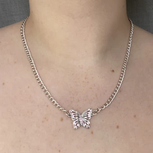 Fjärilshalsband med rosa diamanter | Urban Outfitters - Ett jättegulligt y2k silvrigt fjärilshalsband därfjärilen har rosa diamanter från Urban Outfitters.