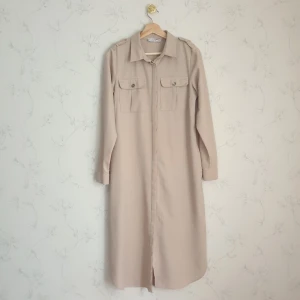 Beige lång skjorta - 🤎FÖRST TILL KVARN🤎 En fin lång beige skjorta. Skön & vardaglig men kan även "kläs upp" om man lägger till ett fint skärp och har med klackar. Finns  knappar i fram fickorna & på ärmarna och även fina detaljer på axlarna. Står 40, men tycker att den sitter som en 38:a på mig iaf, kan skicka mått vid intresse🧚🏻‍♀️