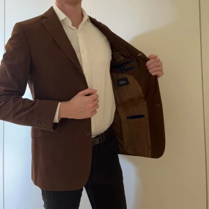 Kavaj Oscar Jacobson Manchester 48 - Trevlig brun kavaj ”Fernando” i manchestertyg (100% bomull) från Ocar Jacobson. Använd ca 5 gånger. Ser ut som ny. Storlek 48. Treknäppt och enkel sprund.
