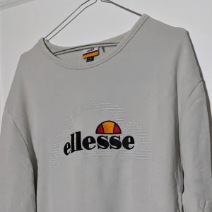 Ellesse collage sweater - Retro collage sweater från Ellesse! Så snygg med motiv framtill och remsa på sidorna under ärmarna. Använt skick och med en bläckfläck vid kragen baktill. Därav priset! 