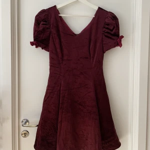 Röd sammetsklänning med rosetter - Vinröd sammetsklänning som framhäver midja. Rosetter på armarna
