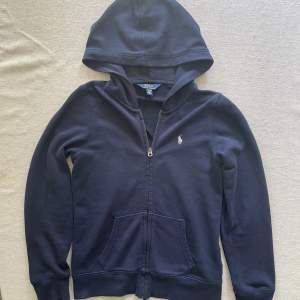 Det är en blå polo Ralph lauren zip hoodie. Den är barnstorlek 12 år/156cm. Jag skulle säga att den passar 164cm. Den är sparsamt använd och är i nyskick.Den är köpt från boozt.com för 1195kr.