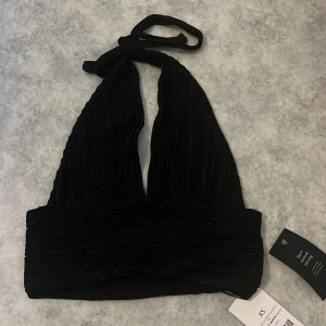 Svart glittrig topp - Säljer en svart glittrig halterneck topp från NA-KD i storlek ca då den är för liten för mig. Den är aldrig använd och har prislappen kvar. (Köparen står för frakt)🩷