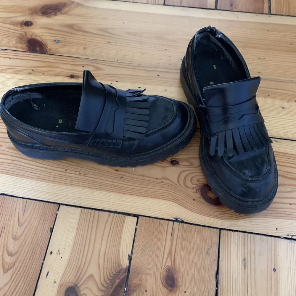 Black faux leather loafers with a small platform and fringe  . Skor.