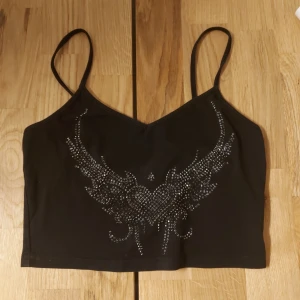 Kort svart linne - Croppat v-cut linne med rhinestonepärlor. Använt men i fint skick. Hund finns i hemmet