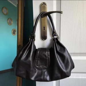 Brun axelväska - Supersöt brun axelväska, har tre fack varav två går att stänga med magnet och det i mitten med dragkedja (har även ett litet plånboksfack med dragkedja). Rymlig och sjukt snygg, den är brun men ser mörkare ut på bilden💕