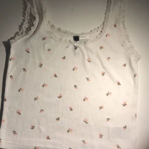 Vit, blommig crop top - Ett vitt linne med spets och blommönster från hm. Är i bra skick och bara använd ett fåtal gång. 