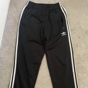 Adidas trackpants  - Adidas byxor glansiga, knappt använda, de en bakficka o två fick med dragkedja i fram. Dom är raka i benen.