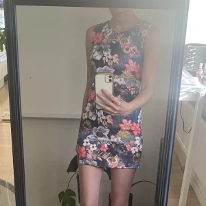 Blommig festklänning  - Snygg festklänning som är sparsamt använd. Skönt material och snygg öppning i ryggen och klänningen är ungefär 77 cm lång. 