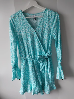 Blå blommig playsuit - En blå blommig playsuit (är med shorts) har knyte i midjan och indragen vid handledarna.  Aldrig använd. Från New Yorker i storlek Xs.