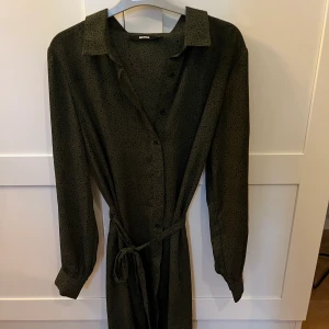 Klänning - Mörkgrön med svarta leopard prickar från Bikbok med knappar och ett snöre i midjan som kan välja att ha på eller inte.