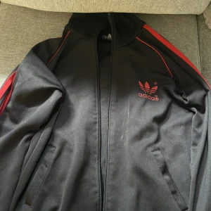 Adidasjacka - Skitsnygg adidas jacka i svart och rött! Den är knappt använd men dragkedjan är lite trasig men den går fortfarande att knäppa!