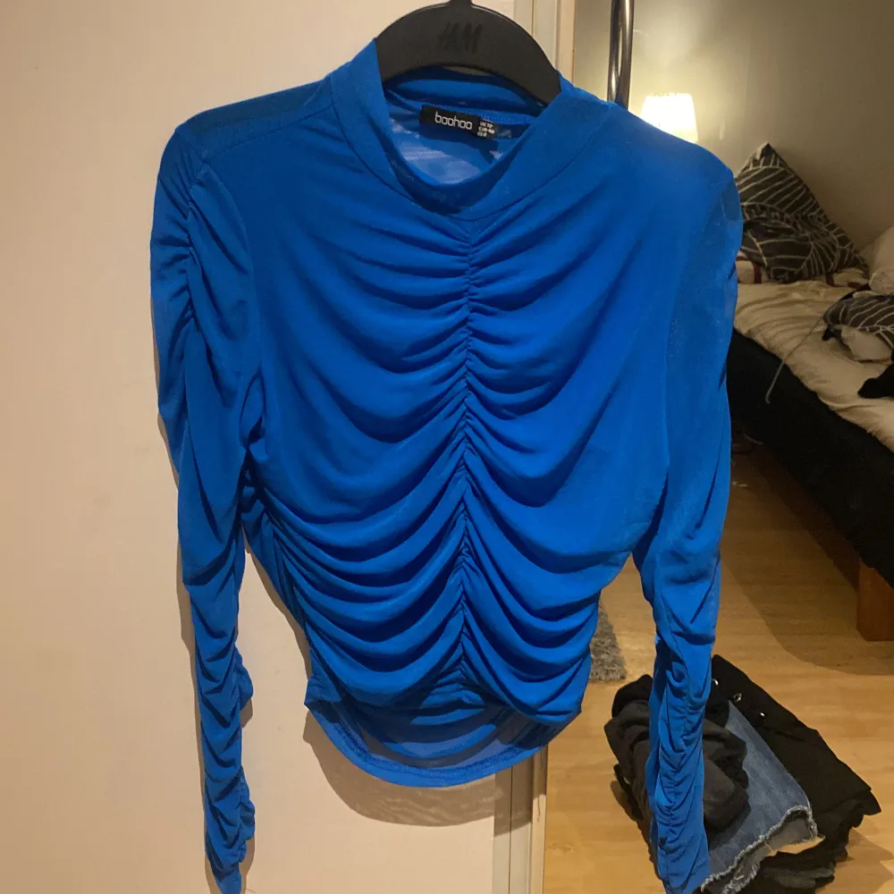 Rynkad, blå tröja från Boohoo typ i mesh. Framsidan är i dubbelt tyg, ryggen och ärmarna i enkelt så de är väldigt genomskinliga. Står strl 40, upplever den som en S eller M då den är stretchig.. Toppar.