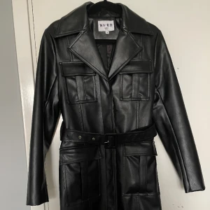 Lång läderkappa  - En lång läderjacka i fakeskinn, storlek 36 från NAKD. Skärpet är avtagbart