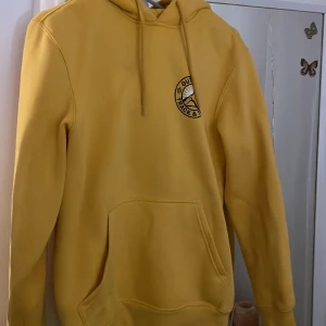 Gul hoodie - Gul hoodie med tryck på bröstet & ryggen. Liten fläck men snöret täcker över det mesta (se bild 2)