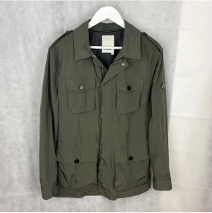 J.Lindberg Safari Jacka - J.Lindberg Safari Jacka i utmärkt skick. Riktigt stilren och perfekt i passformen! Färgen är olivgrön och mycket snygg till höst och vinter. Nypris för jackan är uppemot 4000kr. Jackan är använd men inga tecken alls på defekter.