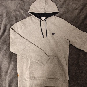 Timberland Hoodie Grå - Säljer nu min helt oanvända Timberland Hoodie eftersom den är för stor för mig. Helt i nyskick, inga defekter. Prislappen är kvar. Nypris 1149kr. Skönt material. Bara att höra av sig vid minsta fundering och pris går alltid att diskuteras vid snabb affär.