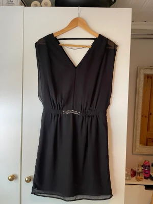 Klänning - Svart klänning med smycke i midjan. Storlek: 36. Lite använd. 